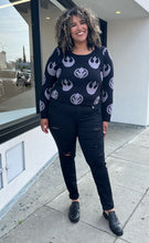 Load image into Gallery viewer, Full-body front view of a pair of size 18 Torrid black distressed skinny jeans styled with a black and gray sweater and black loafers on a size 16/18 model. The photo is taken outside in natural lighting.
