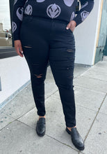 Load image into Gallery viewer, Front view of a pair of size 18 Torrid black distressed skinny jeans styled with a black and gray sweater and black loafers on a size 16/18 model. The photo is taken outside in natural lighting.
