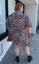 Load image into Gallery viewer, Full-body back view of a size 28 (fits like 24/26) Simply Be pink, blue, orange, white, and black leopard pattern faux wrap mini dress with a tulip hem styled with black boots on a size 22/24 model. The photo is taken outside in natural lighting.
