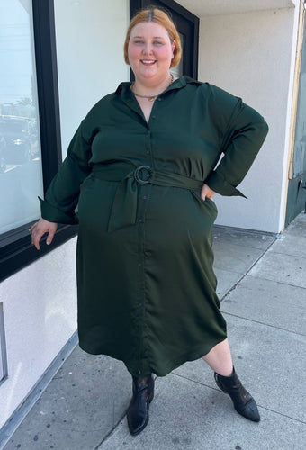 Full-body front view of a size 26 Eloquii emerald green maxi shirt dress with an o-ring fabric belt styled with black boots on a size 22/24 model. The photo is taken outside in natural lighting.