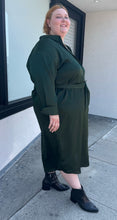 Load image into Gallery viewer, Full-body side view of a size 26 Eloquii emerald green maxi shirt dress with an o-ring fabric belt styled with black boots on a size 22/24 model. The photo is taken outside in natural lighting.
