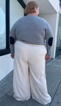 Load image into Gallery viewer, Full-body back view of a size 26 Eloquii off-white cargo-style wide leg trouser styled with a gray sweater and black slides on a size 22/4 model. The photo is taken outside in natural lighting.
