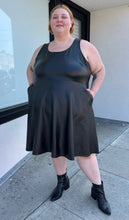 Load image into Gallery viewer, Additional full-body front view of a size 4 Torrid black pleather tank-style a-line midi dress with pockets styled with black boots on a size 22/24 model. The photo is taken outside in natural lighting.
