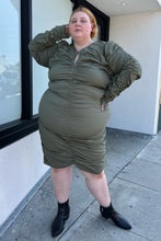 Load image into Gallery viewer, Full-body front view of a size 4 Fashion to Figure army green all-over ruched long sleeve midi dress with keyhole bust detail styled with black boots on a size 22/24 model. The photo is taken outside in natural lighting.
