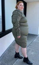 Load image into Gallery viewer, Full-body side view of a size 4 Fashion to Figure army green all-over ruched long sleeve midi dress with keyhole bust detail styled with black boots on a size 22/24 model. The photo is taken outside in natural lighting.
