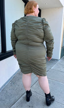 Load image into Gallery viewer, Full-body back view of a size 4 Fashion to Figure army green all-over ruched long sleeve midi dress with keyhole bust detail styled with black boots on a size 22/24 model. The photo is taken outside in natural lighting.

