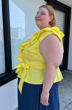 Load image into Gallery viewer, Side view of a size 4 Fashion to Figure x Gabrielle Union collab bright yellow ruffled wrap blouse styled with a denim skirt on a size 22/24 model. The photo is taken outside in natural lighting.

