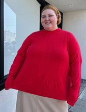 Load image into Gallery viewer, Additional front view showing off the length of a size 4X Roaman&#39;s red ribbed knot mockneck sweater styled with a khaki skirt on a size 22/4 model. The photo is taken outside in natural lighting.
