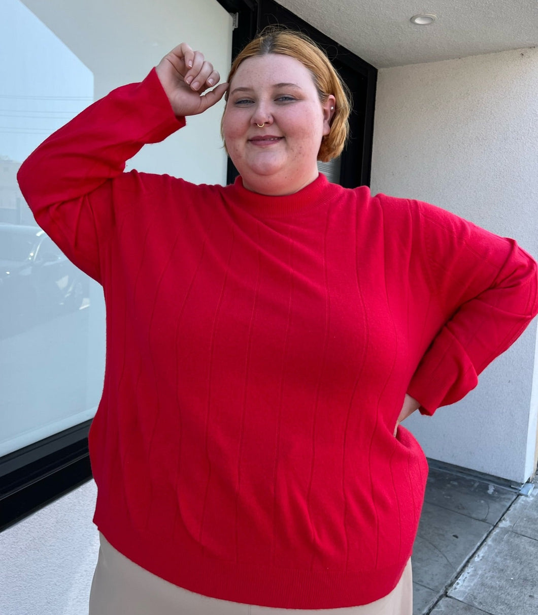 Front view of a size 4X Roaman's red ribbed knot mockneck sweater styled with a khaki skirt on a size 22/4 model. The photo is taken outside in natural lighting.