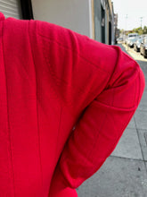 Load image into Gallery viewer, Close up view of the ribbing and knit pattern of a size 4X Roaman&#39;s red ribbed knot mockneck sweater on a size 22/4 model. The photo is taken outside in natural lighting.
