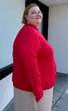 Load image into Gallery viewer, Side view of a size 4X Roaman&#39;s red ribbed knot mockneck sweater styled with a khaki skirt on a size 22/4 model. The photo is taken outside in natural lighting.
