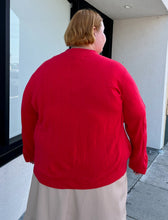 Load image into Gallery viewer, Back view of a size 4X Roaman&#39;s red ribbed knot mockneck sweater styled with a khaki skirt on a size 22/4 model. The photo is taken outside in natural lighting.
