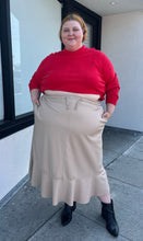 Load image into Gallery viewer, Full-body front view of a size 24/26 Ulla Popken khaki maxi skirt with drawstring waist and ruffle hem styled with a red sweater and black boots on a size 22/24 model. The photo is taken outside in natural lighting.
