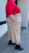 Load image into Gallery viewer, Side view of a size 24/26 Ulla Popken khaki maxi skirt with drawstring waist and ruffle hem styled with a red sweater and black boots on a size 22/24 model. The photo is taken outside in natural lighting.
