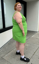 Load image into Gallery viewer, Full-body side view of a size 24 ASOS lime green mini sheath dress with a small slit at the hem styled with black mary janes on a size 22/24 model. The photo is taken outside in natural lighting.
