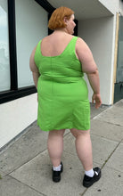 Load image into Gallery viewer, Full-body back view of a size 24 ASOS lime green mini sheath dress with a small slit at the hem styled with black mary janes on a size 22/24 model. The photo is taken outside in natural lighting.
