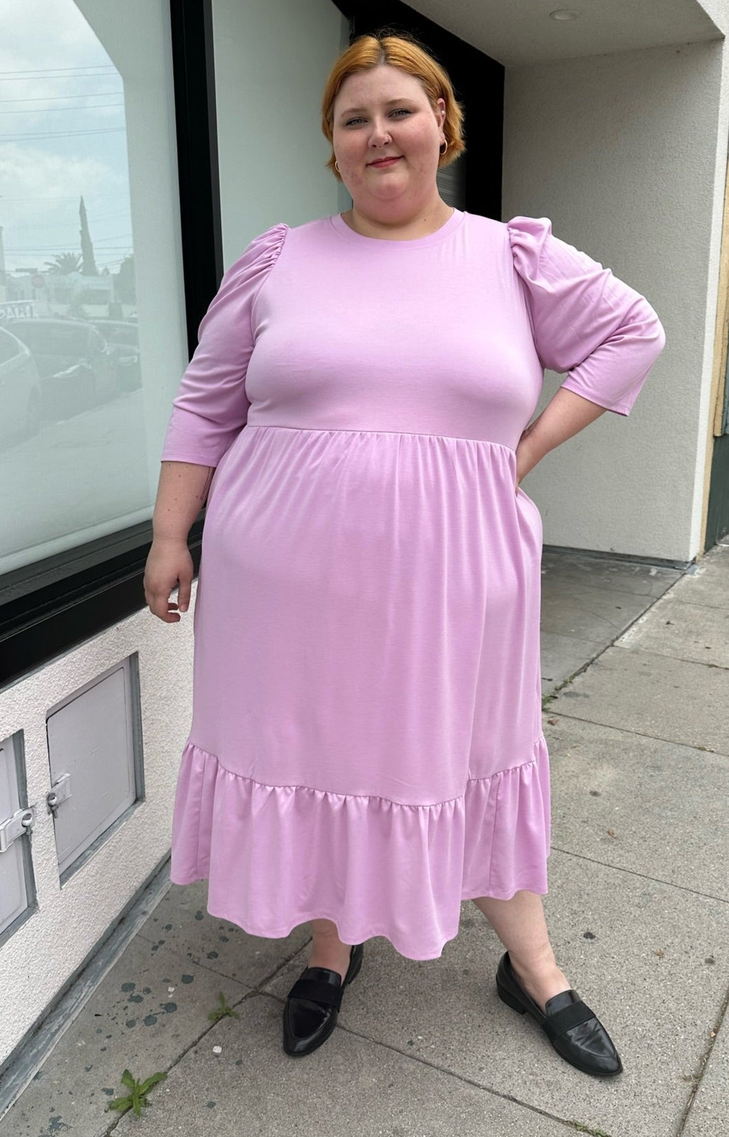 Full-body front view of a size 2X Who What Wear light pink puff sleeve maxi dress with a ruffled hem styled with black slides on a size 22/24 model. The photo is taken outside in natural lighting.