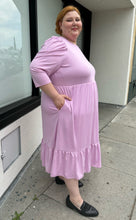 Load image into Gallery viewer, Full-body side view showing off the pockets of a size 2X Who What Wear light pink puff sleeve maxi dress with a ruffled hem styled with black slides on a size 22/24 model. The photo is taken outside in natural lighting.
