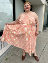 Load image into Gallery viewer, Additional full-body front view of a size 5X WRAY NYC orange and white checkered windowpane tank maxi dress with tie belt styled with brown mules on a size 22/24 model. The photo is taken outside in natural lighting.
