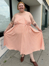 Load image into Gallery viewer, Full-body front view of a size 5X WRAY NYC orange and white checkered windowpane tank maxi dress with tie belt styled with brown mules on a size 22/24 model. The photo is taken outside in natural lighting.
