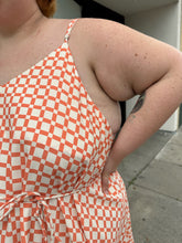 Load image into Gallery viewer, Close view of the adjustable straps and checkered windowpane pattern of a size 5X WRAY NYC orange and white checkered windowpane tank maxi dress with tie belt on a size 22/24 model. The photo is taken outside in natural lighting.
