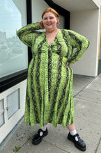 Load image into Gallery viewer, Additional full-body front view of a size 26 ASOS lime green and black snake patterned maxi with twist-front tie detail and long sleeves styled with black mary janes on a size 22/24 model.. The photo is taken outside in natural lighting.
