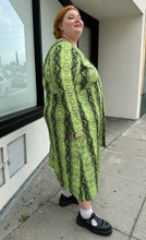 Load image into Gallery viewer, Full-body side view of a size 26 ASOS lime green and black snake patterned maxi with twist-front tie detail and long sleeves styled with black mary janes on a size 22/24 model.. The photo is taken outside in natural lighting.
