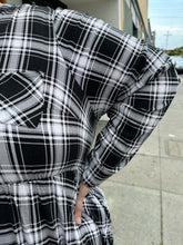 Load image into Gallery viewer, Close up view of the plaid pattern and breast pockets of a size 3 Torrid black and white plaid collarless a-line shirt dress with breast pockets on a size 22/24 model. The photo is taken outside in natural lighting.
