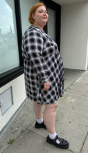Load image into Gallery viewer, Full-body side view of a size 3 Torrid black and white plaid collarless a-line shirt dress with breast pockets styled with black mary janes on a size 22/24 model. The photo is taken outside in natural lighting.
