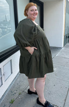 Load image into Gallery viewer, Full-body side view of a size 3X A New Day olive green square neck puff sleeve tiered dress styled with black slides on a size 22/24 model. The photo is taken outside in natural lighting.
