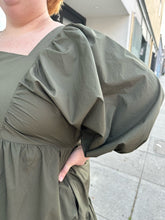 Load image into Gallery viewer, Close up view of the voluminous puff sleeve of a size 3X A New Day olive green square neck puff sleeve tiered dress on a size 22/24 model. The photo is taken outside in natural lighting.
