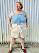 Load image into Gallery viewer, Full-body front view of a size 4X Old Navy cream khaki shorts with tie belt styled with a light blue tank tucked in and brown mules on a size 22/24 model. The photo is taken outside in natural lighting.
