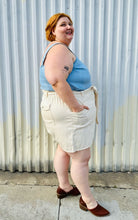 Load image into Gallery viewer, Full-body side view of a size 4X Old Navy cream khaki shorts with tie belt styled with a light blue tank tucked in and brown mules on a size 22/24 model. The photo is taken outside in natural lighting.
