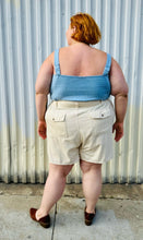 Load image into Gallery viewer, Full-body back view of a size 4X Old Navy cream khaki shorts with tie belt styled with a light blue tank tucked in and brown mules on a size 22/24 model. The photo is taken outside in natural lighting.
