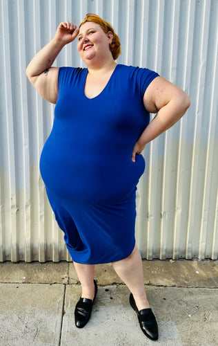 Full-body front view of a size M (Universal Standard size 18/20) royal blue v-neck t-shirt dress styled with black loafer slides on a size 22/24 model. The photo is taken outside in natural lighting.