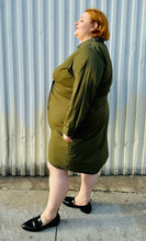 Load image into Gallery viewer, Full-body side view of a size 4 Fashion to Figure army green twist-front collared shirt dress styled with black slide loafers on a size 22/24 model. The photo is taken outside in natural lighting.
