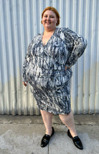 Load image into Gallery viewer, Additional full-body front view of a size 4X Tart black, blue, and white abstract tie dye long sleeve faux wrap dress styled with black loafer slides on a size 22/24 model. The photo is taken outside in natural lighting.
