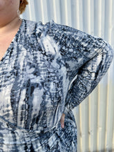 Load image into Gallery viewer, Close up view of the blue, black, and white abstract tie dye of a size 4X Tart black, blue, and white abstract tie dye long sleeve faux wrap dress on a size 22/24 model. The photo is taken outside in natural lighting.
