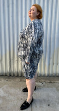 Load image into Gallery viewer, Full-body side view of a size 4X Tart black, blue, and white abstract tie dye long sleeve faux wrap dress styled with black loafer slides on a size 22/24 model. The photo is taken outside in natural lighting.
