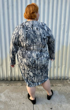 Load image into Gallery viewer, Full-body back view of a size 4X Tart black, blue, and white abstract tie dye long sleeve faux wrap dress styled with black loafer slides on a size 22/24 model. The photo is taken outside in natural lighting.
