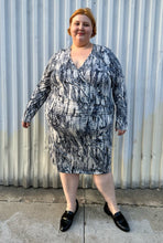 Load image into Gallery viewer, Full-body front view of a size 4X Tart black, blue, and white abstract tie dye long sleeve faux wrap dress styled with black loafer slides on a size 22/24 model. The photo is taken outside in natural lighting.
