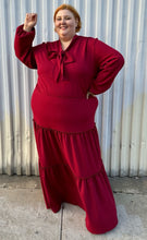 Load image into Gallery viewer, Full-body front view showing off the subtle puff sleeves of a size 3X Melissa Masse Made to Measure deep red tiered maxi dress with subtle long puff sleeves, pussy bow neckline, and long tiers on a size 22/24 model. The photo is taken outside in natural lighting.
