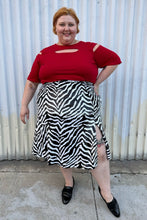 Load image into Gallery viewer, Full-body front view of a size 22 Novella black and white sequin zebra pattern maxi skirt with side slit styled with a red top and black loafer slides on a size 22/24 model. The photo is taken outside in natural lighting.
