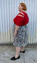 Load image into Gallery viewer, Full-body side view of a size 22 Novella black and white sequin zebra pattern maxi skirt with side slit styled with a red top and black loafer slides on a size 22/24 model. The photo is taken outside in natural lighting.
