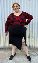 Load image into Gallery viewer, Additional full-body front view of a size 22/24 Eloquii black and red leopard pattern long sleeve bodysuit styled tucked into a black high-slit skirt and black loafer slides on a size 22/24 model. The photo is taken outside in natural lighting.
