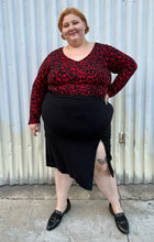 Load image into Gallery viewer, Additional full-body front view of a size 26 Lane Bryant black stretchy midi skirt with convertible high side slit styled with a red &amp; black leopard bodysuit and black loafers on a size 22/24 model. The photo is taken outside in natural lighting.
