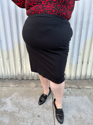 Front view of a size 26 Lane Bryant black stretchy midi skirt with convertible high side slit styled with a red & black leopard bodysuit and black loafers on a size 22/24 model. The photo is taken outside in natural lighting.