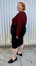 Load image into Gallery viewer, Full-body side view of a size 22/24 Eloquii black and red leopard pattern long sleeve bodysuit styled tucked into a black high-slit skirt and black loafer slides on a size 22/24 model. The photo is taken outside in natural lighting.
