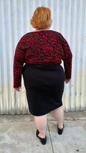 Load image into Gallery viewer, Full-body back view of a size 22/24 Eloquii black and red leopard pattern long sleeve bodysuit styled tucked into a black high-slit skirt and black loafer slides on a size 22/24 model. The photo is taken outside in natural lighting.
