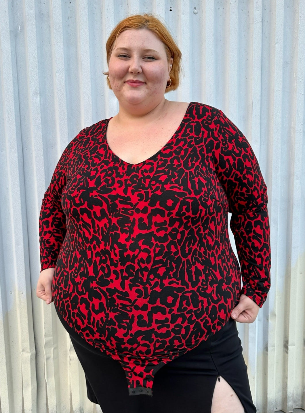 Front view of a size 22/24 Eloquii black and red leopard pattern long sleeve bodysuit on a size 22/24 model. The photo is taken outside in natural lighting.